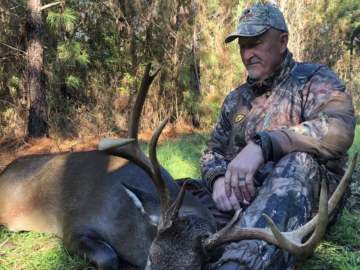 A hunter sitting with a mature whitetail buck in Georgia pine woods