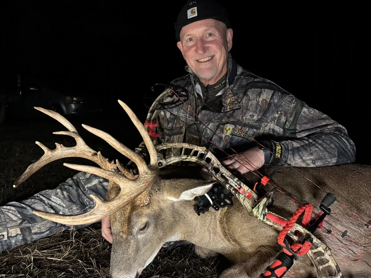 A bowhunter kneeling behind a mature whitetail buck taken after dark