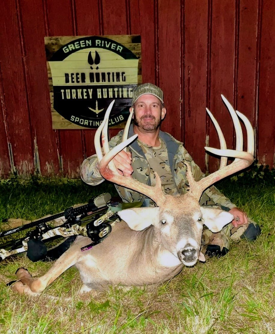 Hunter with a heavy-racked buck under the Green River Sportsman Club sign