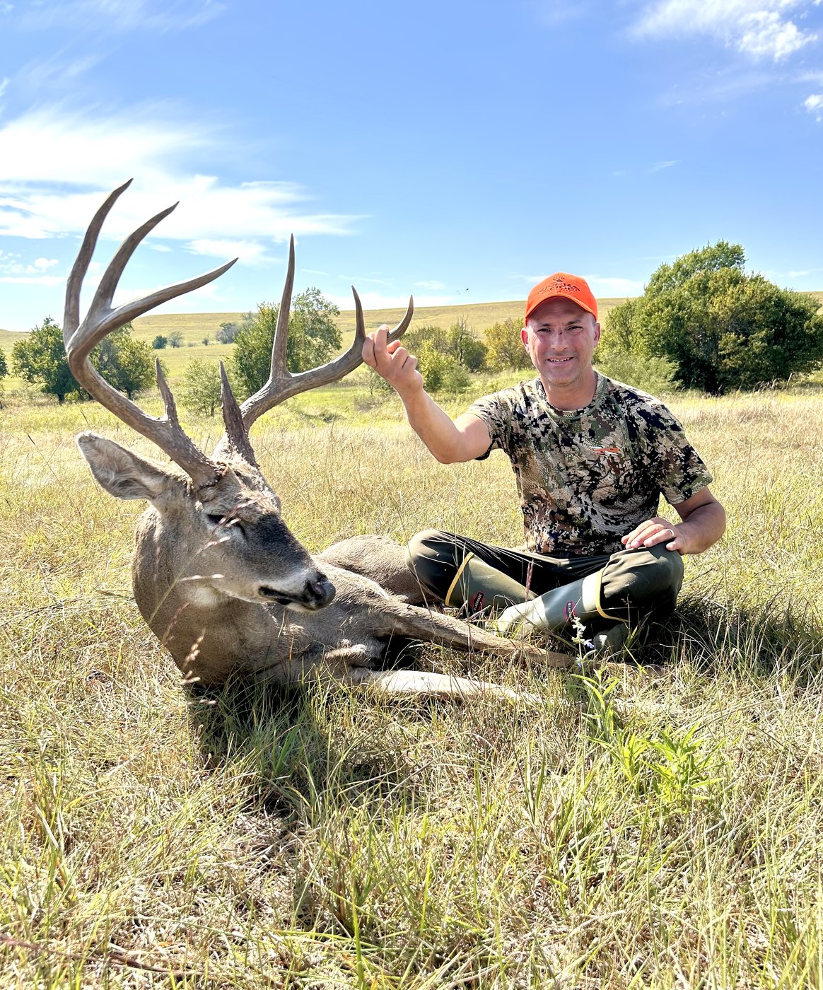 Two hunters behind a wide-racked buck on an open field
