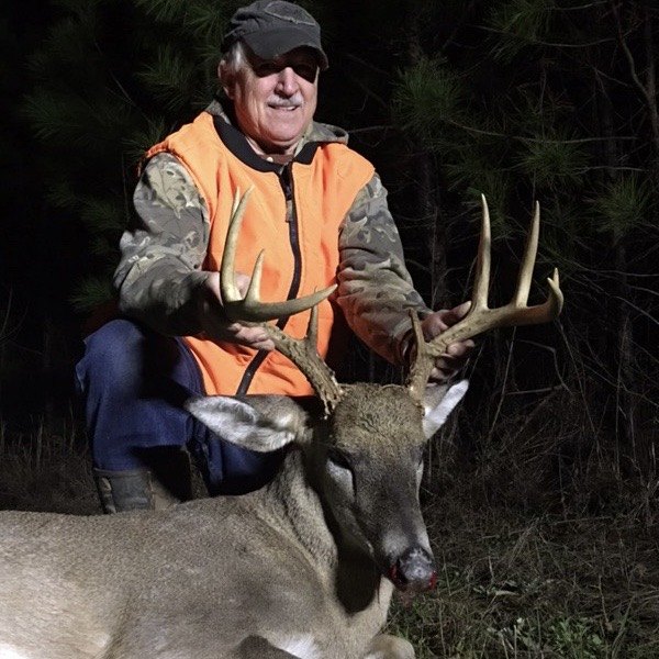 Hunter in blaze orange with a whitetail buck at dusk