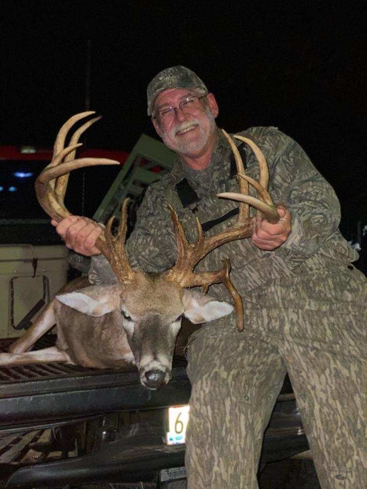 Hunter with a wide-racked buck in a truck bed at night