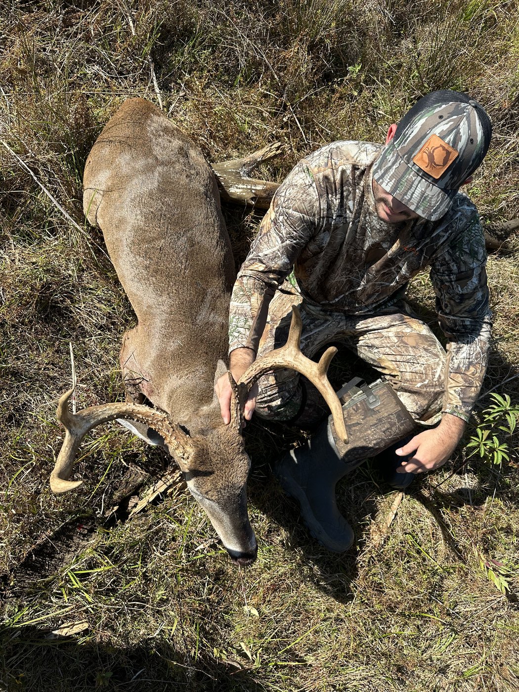 Hunter kneeling behind a buck in leaf litter