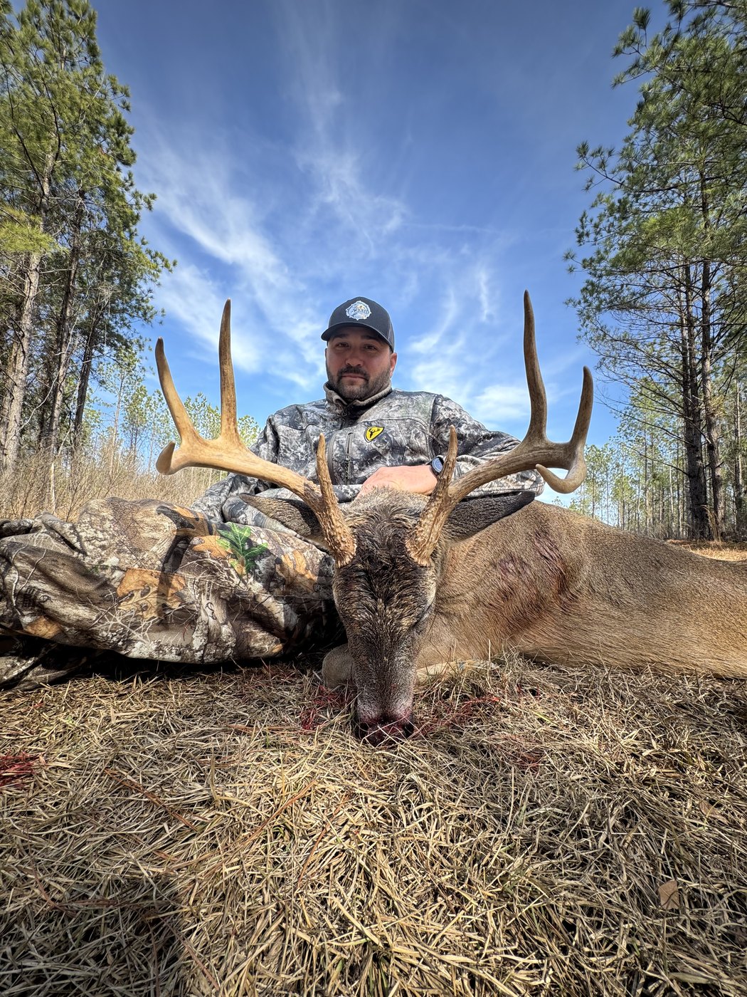 Hunter with a heavy-racked buck under a blue sky