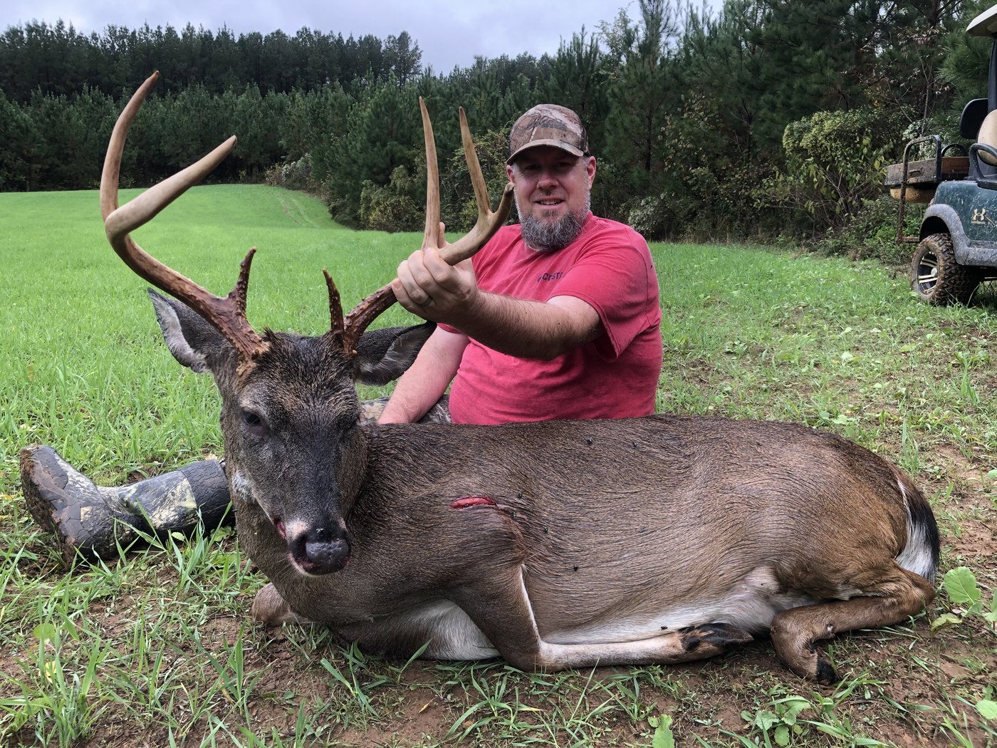 Hunter in a red shirt with a buck on a green field