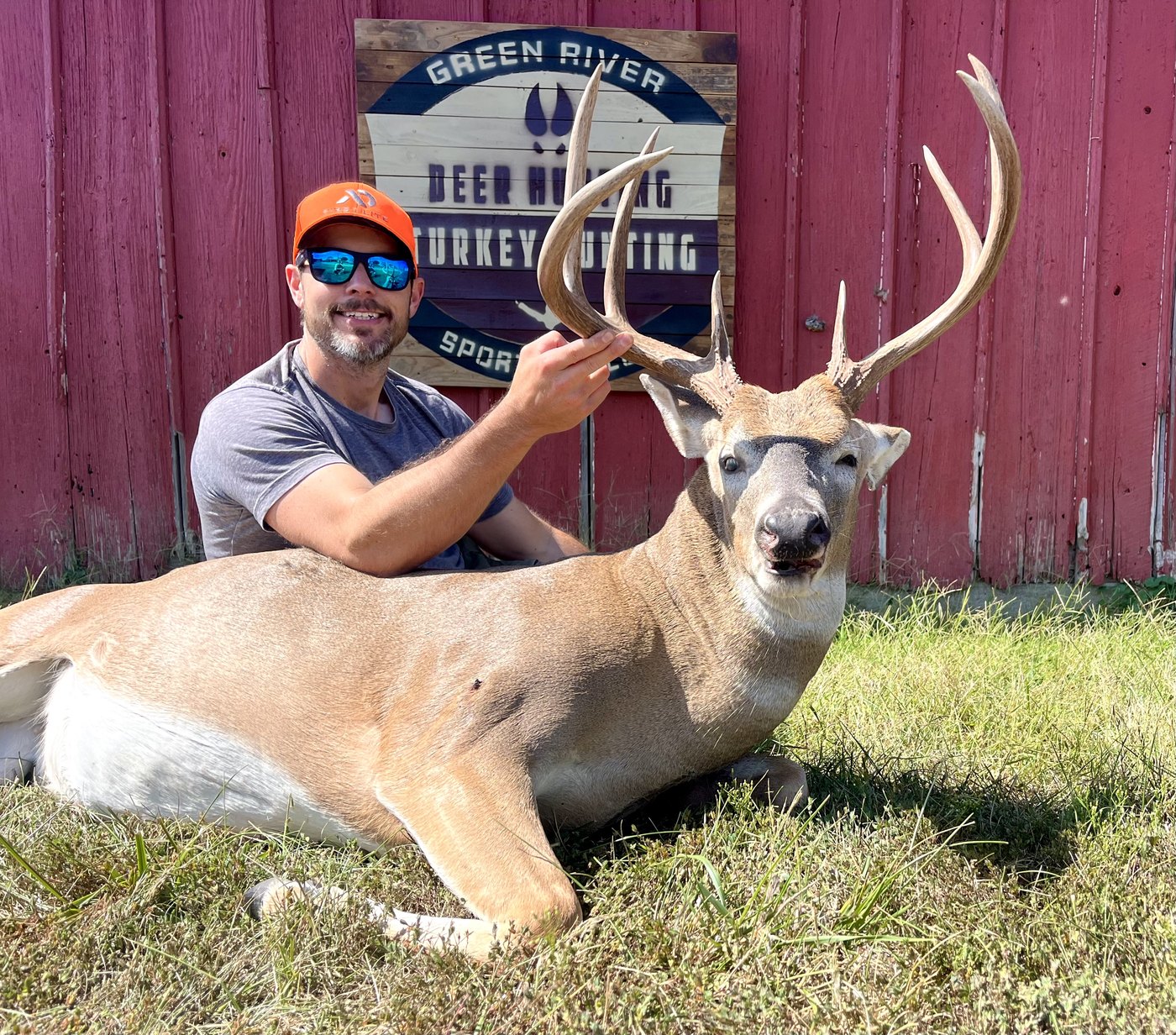 Hunter with a heavy buck under the Green River Sportsman Club sign