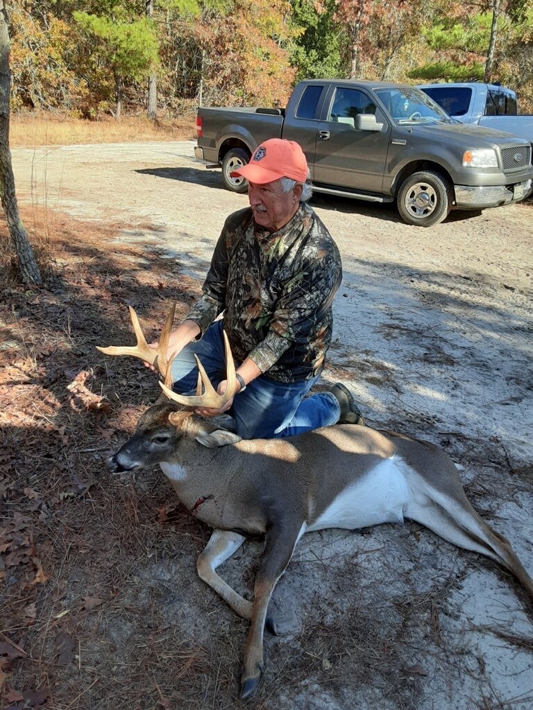 Hunter with a buck beside a truck on a woods road