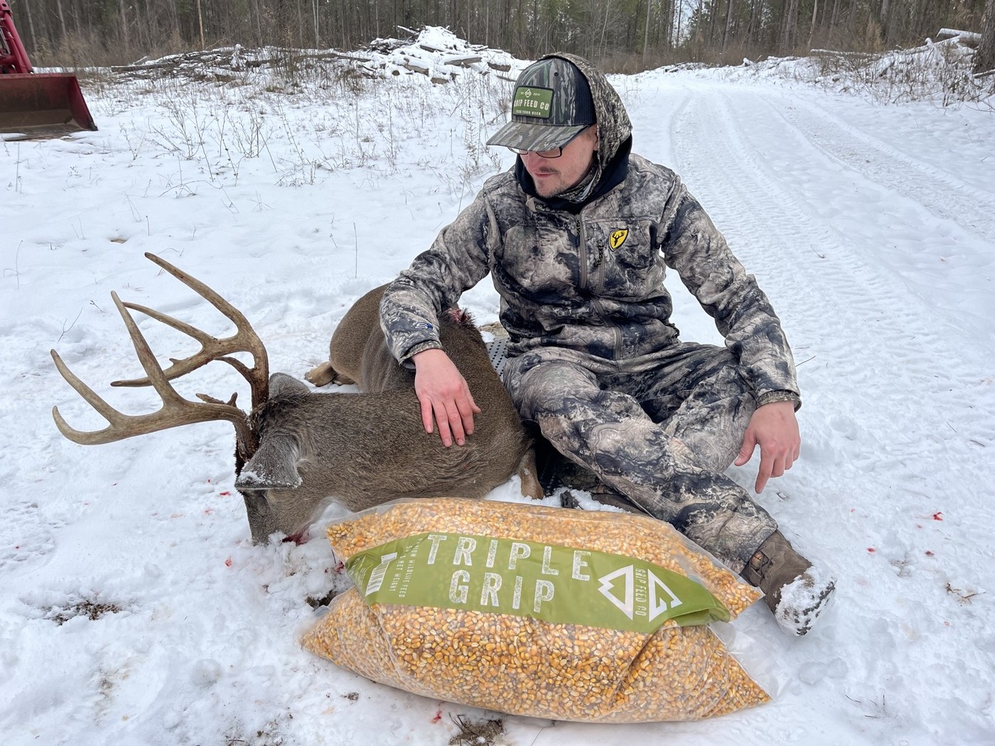 Hunter with a whitetail buck beside a bag of Triple Grip in the snow
