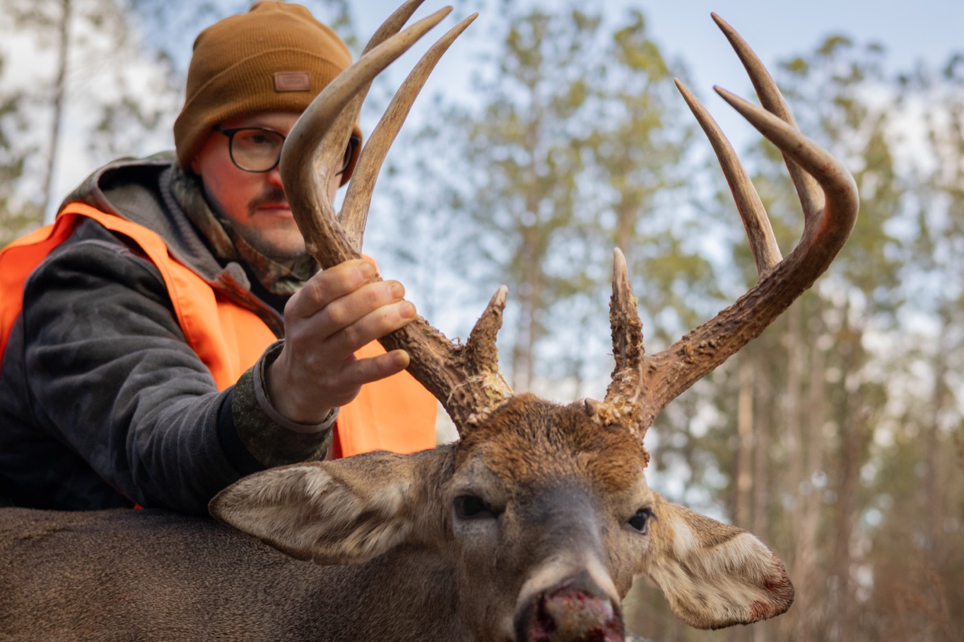 Hunter lifting the antlers of a tall-tined whitetail buck